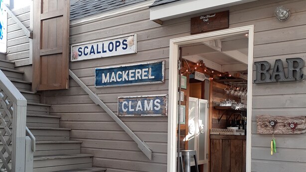 A wooden staircase leading to a bar area with signs for 'SCALLOPS,' 'MACKEREL,' and 'CLAMS.'