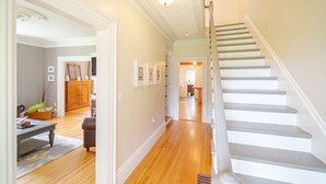 A spacious hallway with a wooden floor leading to a staircase with white balusters and a handrail.