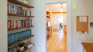A hallway with wooden shelves filled with books, a kitchen area with wooden cabinets, and a bulletin board on the wall.