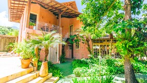 A two-story building with a covered balcony, potted plants, and a well-maintained garden. - VELINN Pousada Villa Caiçara (Ilhabela)