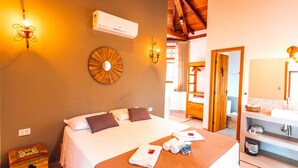A hotel room with a bed, wall-mounted air conditioner, decorative wall art, and a bathroom visible through an open door. - VELINN Pousada Villa Caiçara (Ilhabela)