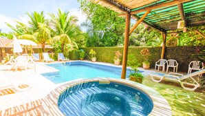 A swimming pool with lounge chairs and a hot tub, surrounded by greenery and a pergola. - VELINN Pousada Villa Caiçara (Ilhabela)