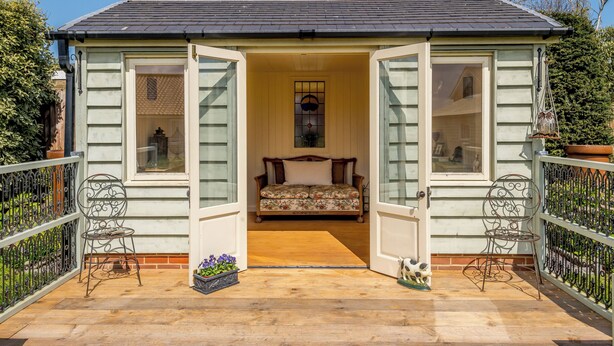 Un acogedor cottage con un porche de madera, una banca y una pequeña mesa adornada con flores.