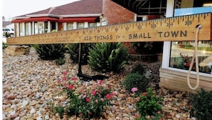 A wooden ruler with the text "BIG THINGS IN A SMALL TOWN" placed in front of a building with a red roof and brick walls. - Park View Place 4 Blocks From the World's Biggest (Casey)
