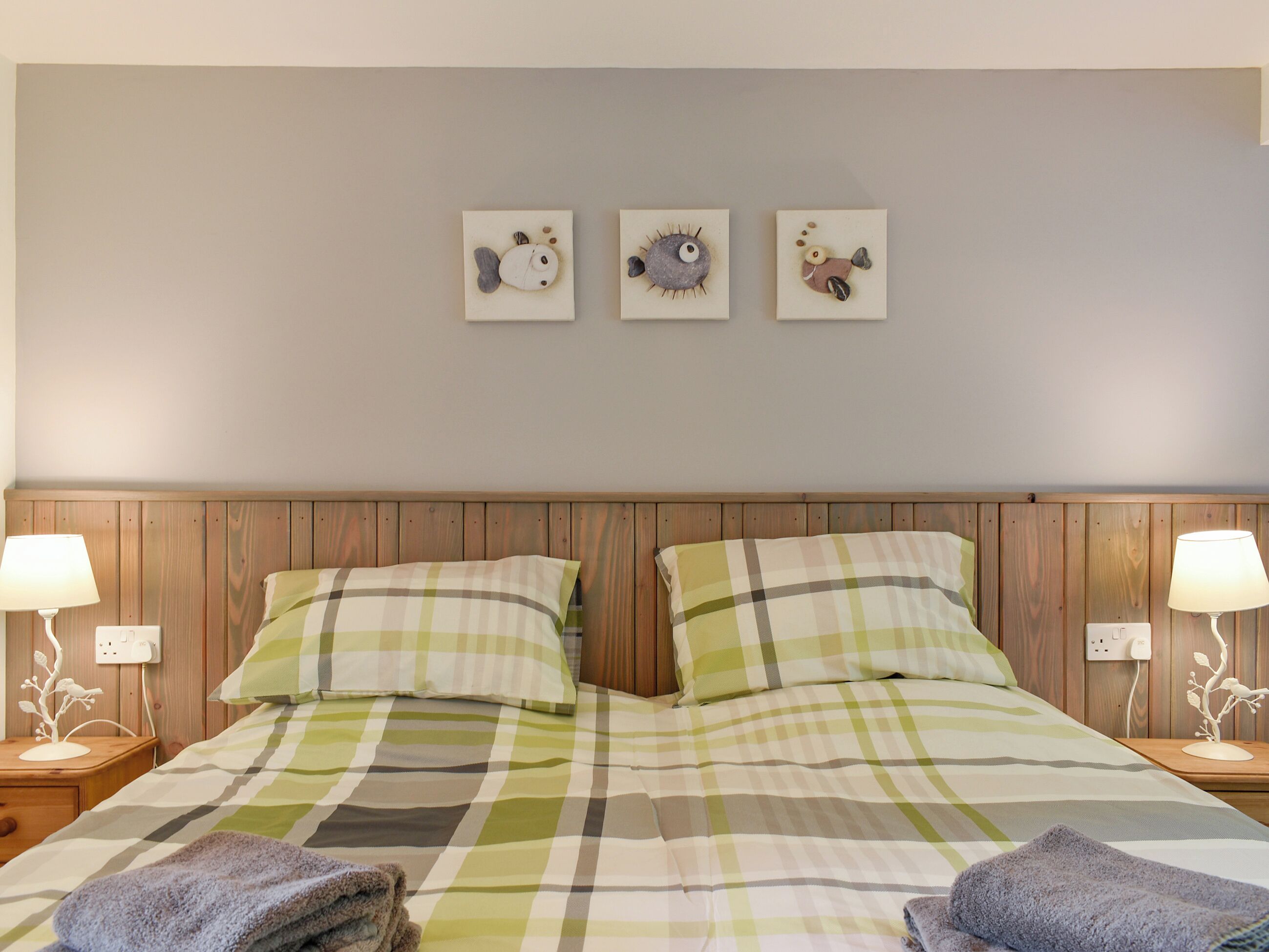 A neatly made bed with a plaid bedspread, two pillows, and two folded towels on the side. There are three wall-mounted decorations above the bed.