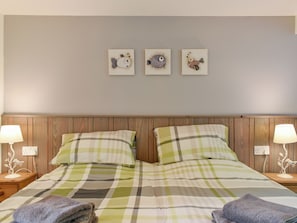 Un lit bien fait, recouvert d’une couverture à carreaux, avec deux oreillers et deux serviettes pliées posées sur le côté. Trois éléments décoratifs sont accrochés au mur au-dessus du lit.