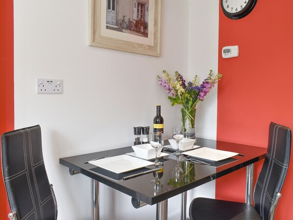 Une table à manger avec des chaises, un tableau encadré, une horloge et un vase avec des fleurs.