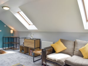 Un salon moderne de style industriel, avec un plafond en pente, une verrière et un coin salon confortable agrémenté d’un canapé en cuir et de coussins.
