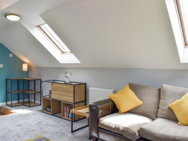 A modern loft-style living room with a sloped ceiling, skylight, and a cozy seating area with a leather sofa and cushions.