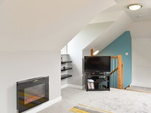 Un salon moderne avec une cheminée, un téléviseur posé sur un meuble en bois et un escalier aux murs de couleur turquoise.