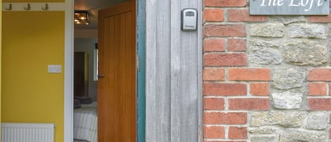 Una puerta de madera que da a una habitación con una cama y un radiador. Un cartel en la pared dice 'The Loft'.
