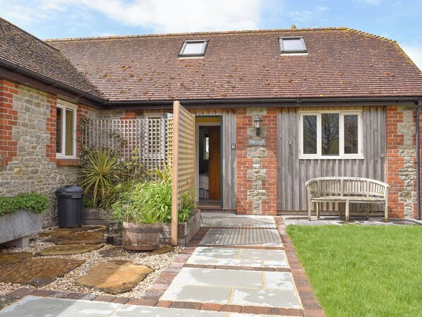 A quaint cottage with a stone facade, a wooden bench, and a small garden area.