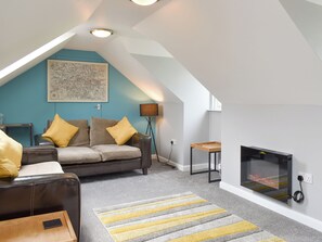 Ein modernes Loft-Apartment mit schrägemausertem Dach, einer gemütlichen Sitzecke mit Sofa und Sesseln, einem kleinen Holztisch, einer Stehlampe und einem Kamin.