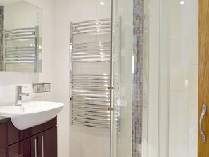 A modern bathroom with a glass shower enclosure, a white sink, and a chrome towel rack.