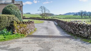 A rural road leading to a stone wall and a house with a well-maintained garden. - Woodend Farmhouse Halmyre (Haugh of Urr, near Castle Douglas)