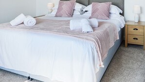 A neatly made bed with a grey headboard, white linens, and pink pillows. There are two bedside tables with lamps and a small drawer. - Woodend Farmhouse Halmyre (Haugh of Urr, near Castle Douglas)