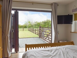 A bedroom with a bed, an open door leading to a grassy outdoor area, a wooden gate, and a television mounted on the wall. - 1 bedroom accommodation in Out Rawcliffe, near Fleetwood (Out Rawcliffe, near Fleetwood)