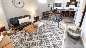 Un salon moderne avec un canapé en cuir noir, un tapis à motifs et une horloge murale aux formes géométriques.