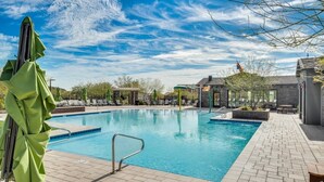 A rectangular swimming pool with a tiled deck, surrounded by lounge chairs and umbrellas. - NEW!!! Spring Break Getaway <br>At Mountain Side Retreat (Buckeye)