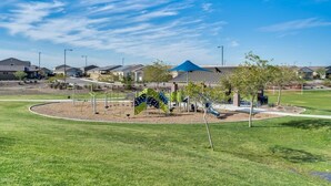 A playground with swings and slides, surrounded by a grassy area and residential buildings in the background. - NEW!!! Spring Break Getaway <br>At Mountain Side Retreat (Buckeye)