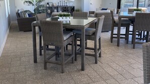 A spacious living area with a dining table surrounded by wicker chairs, a flat-screen TV mounted on the wall, and a large window offering a view of the outdoors. - NEW!!! Spring Break Getaway <br>At Mountain Side Retreat (Buckeye)