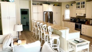 Eine moderne Küche mit weißen Schränken, einer zentralen Kochinsel mit Barhocker und einem Essbereich mit weißem Sofa und Lampe.