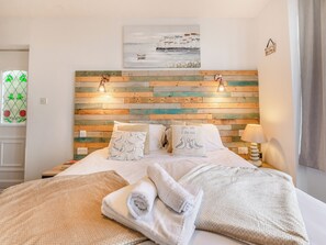 A neatly made bed with pillows, a painting above it, and a wooden headboard.