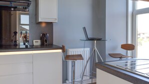 Eine moderne Küche mit einem Laptop auf einem Glastisch, weißen Schränken und einem Fenster.