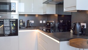 Eine moderne Küche mit weißen Schränken, einem Einbauofen, einer Mikrowelle, einer Kaffeemaschine und einem Toaster.