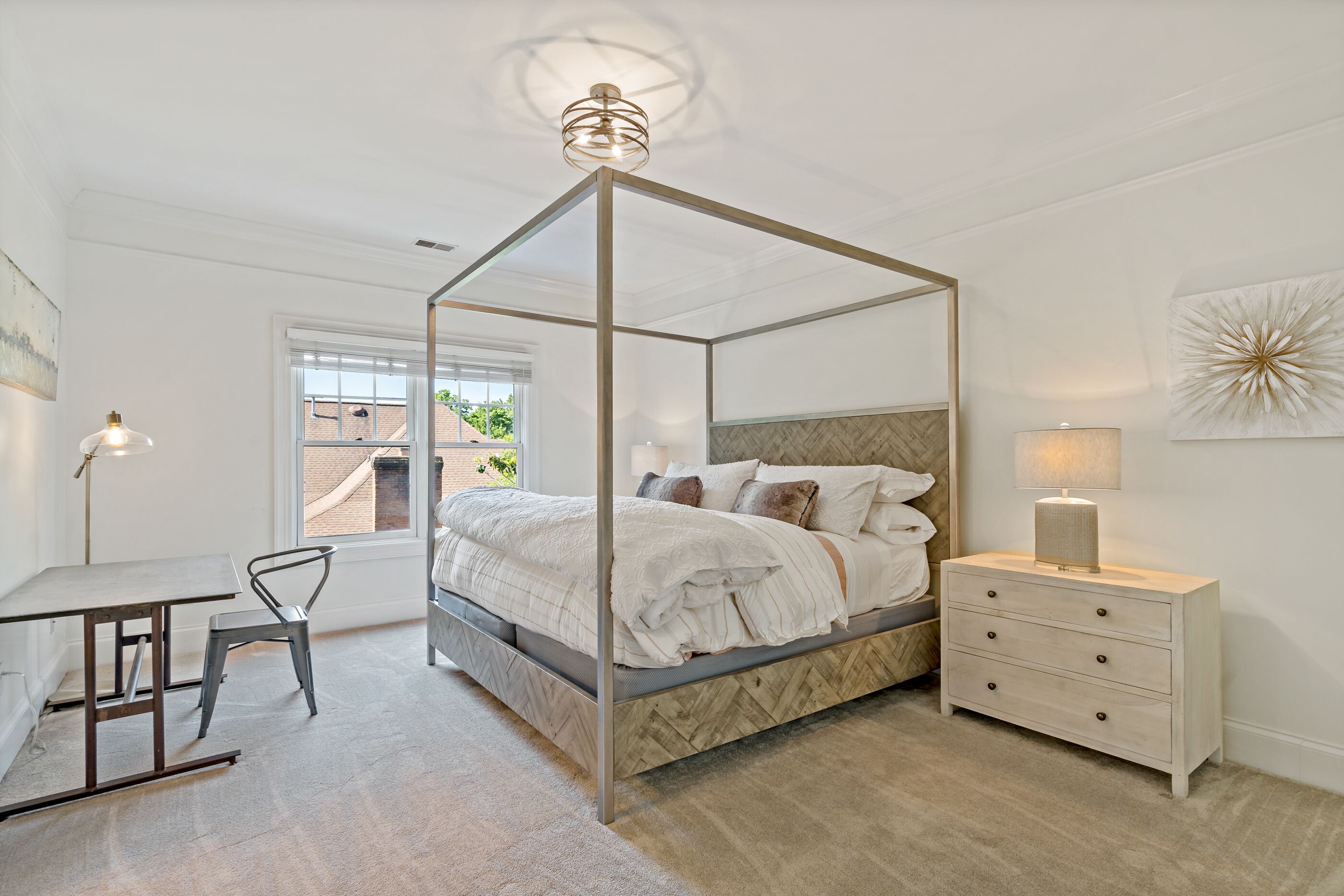 A four-poster bed with a herringbone-patterned headboard, a bedside table with drawers, and a lamp.