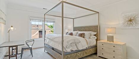 A four-poster bed with a herringbone-patterned headboard, a bedside table with drawers, and a lamp.