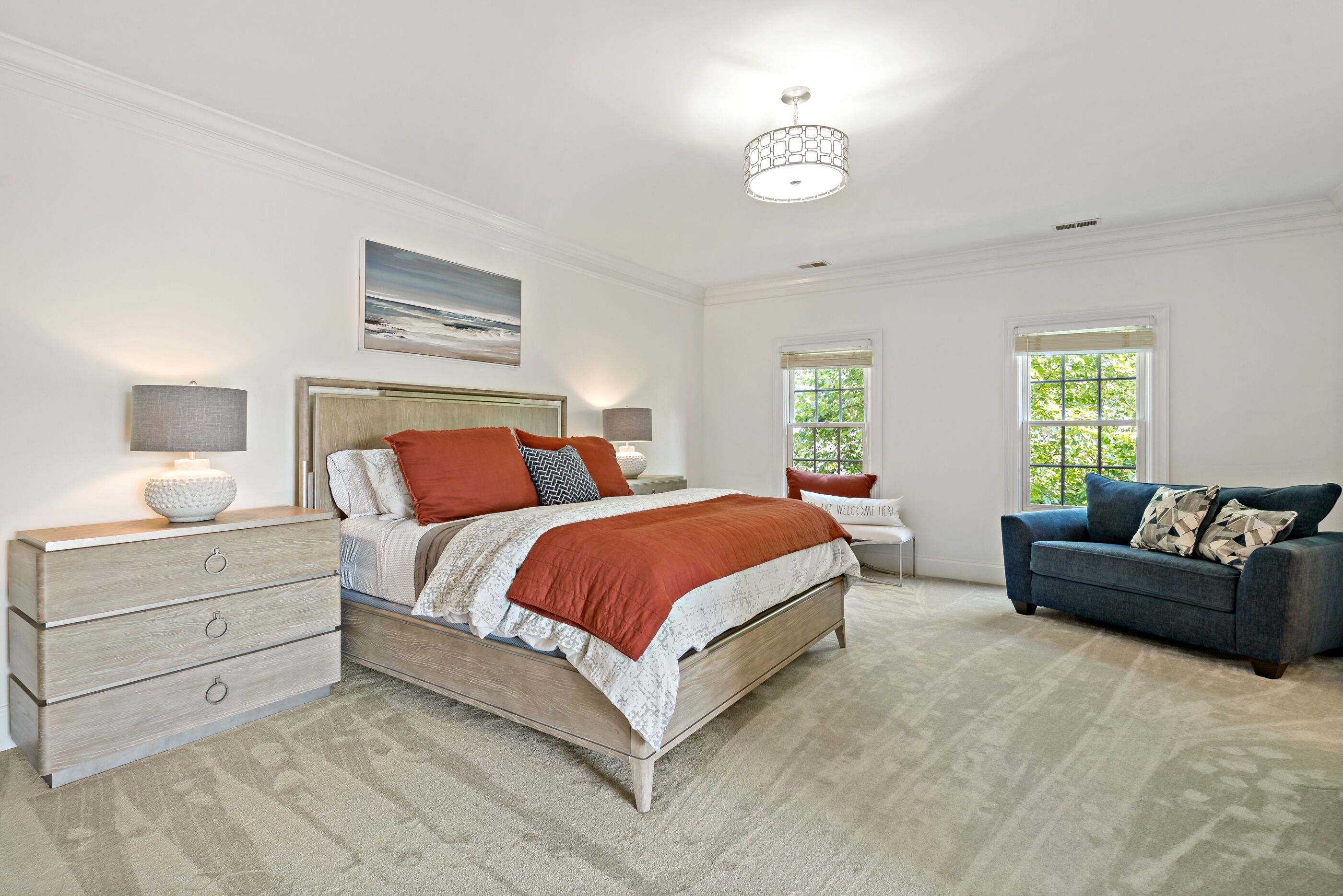 A bedroom with a bed, dresser, nightstands, and a blue sofa.