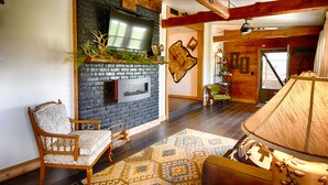 Un soggiorno accogliente con camino, una poltrona comoda, un tappeto decorato e un trave in legno al soffitto.