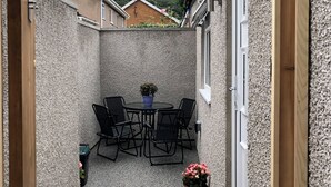 A small outdoor patio with a round table and four chairs, surrounded by a textured wall.