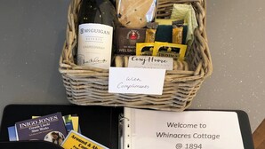 A wicker basket containing a bottle of McGuigan Reserve Chardonnay, a loaf of bread, and some chocolate bars.