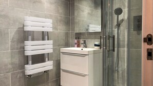 A modern bathroom with a glass shower enclosure, a white vanity with a mirror, and a towel rack.
