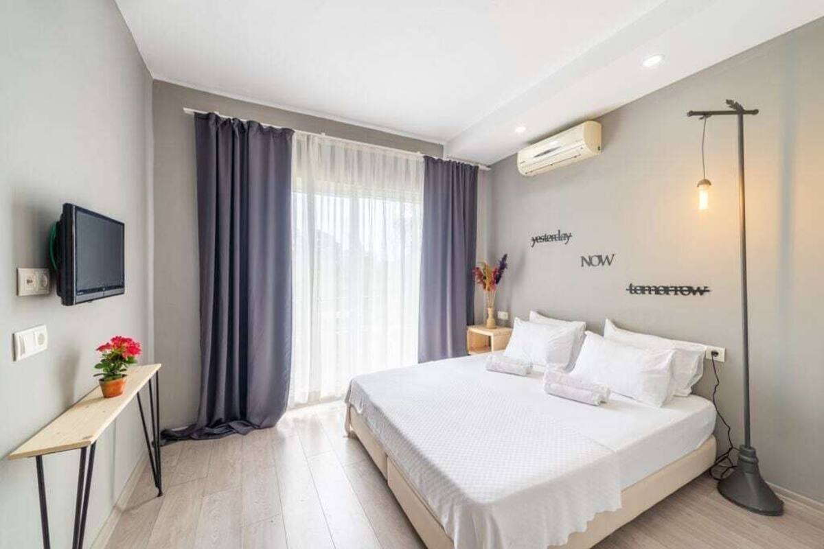 A modern bedroom with a bed, a TV, a bedside table with a plant, and a wall-mounted air conditioner.
