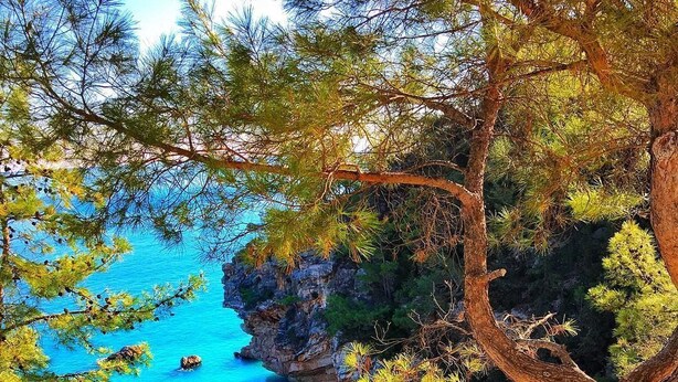 A table with camping gear and two chairs overlooking a beach with clear blue water and rocky cliffs. - Gizli Koy Hotel (Kemer)