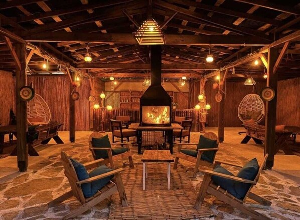 A rustic interior with a central wood-burning stove, stone flooring, and wooden furniture.
