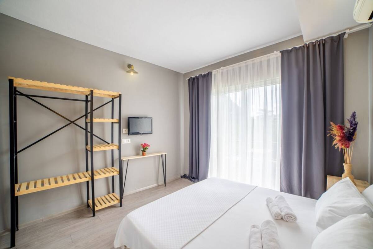 A hotel room with a bed, a TV, a desk, and a wooden rack.