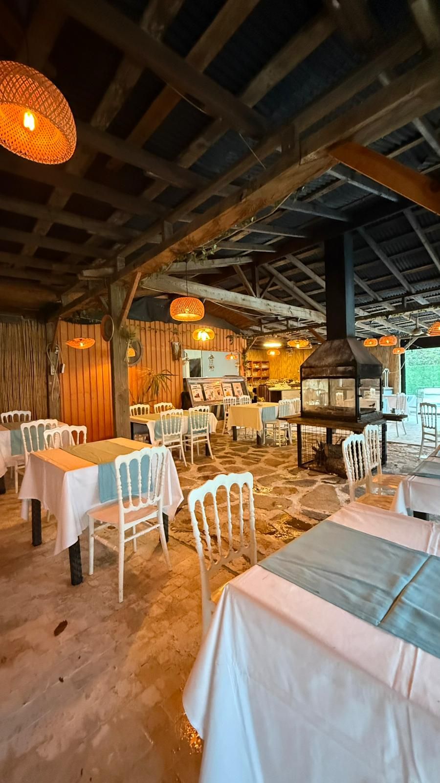 An indoor dining area with tables and chairs, a wooden ceiling, and hanging lights.