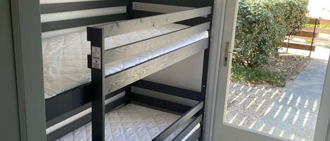 A bunk bed with a white mattress and a small drawer unit.