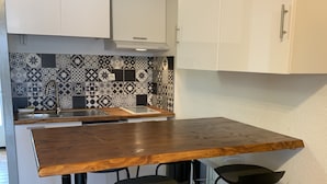 Eine Küche mit Holztisch, zwei schwarzen Hocker, einer Fliesenküchenwand und weißen Schränken.