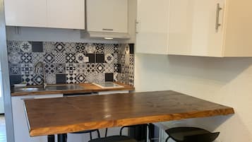 Een keuken met een houten tafel, twee zwarte krukken, een betegelde achterwand en witte kasten.