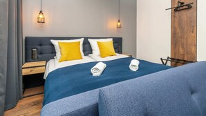 A modern hotel room with a large bed, two bedside tables, and a wooden wardrobe.