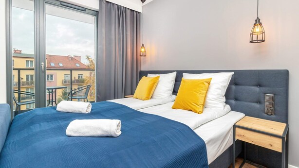 A modern hotel room with a large bed, a bedside table, and a view of the city through large windows.