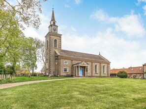 A church with a tall steeple and a clock tower, surrounded by a grassy field and trees.