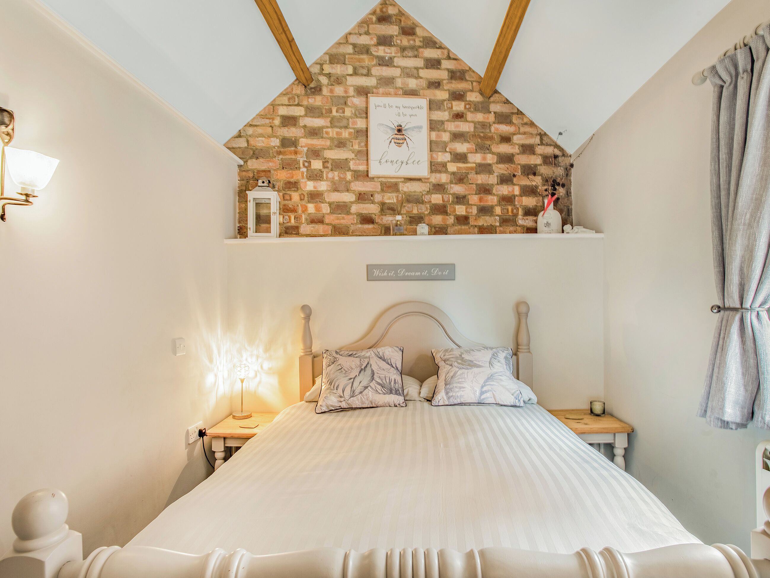 Ein Schlafzimmer mit schräg laufender Decke, einem Bett mit Kopfteil, einem Nachttisch, einer Wandablage und einem Wandzeichen.