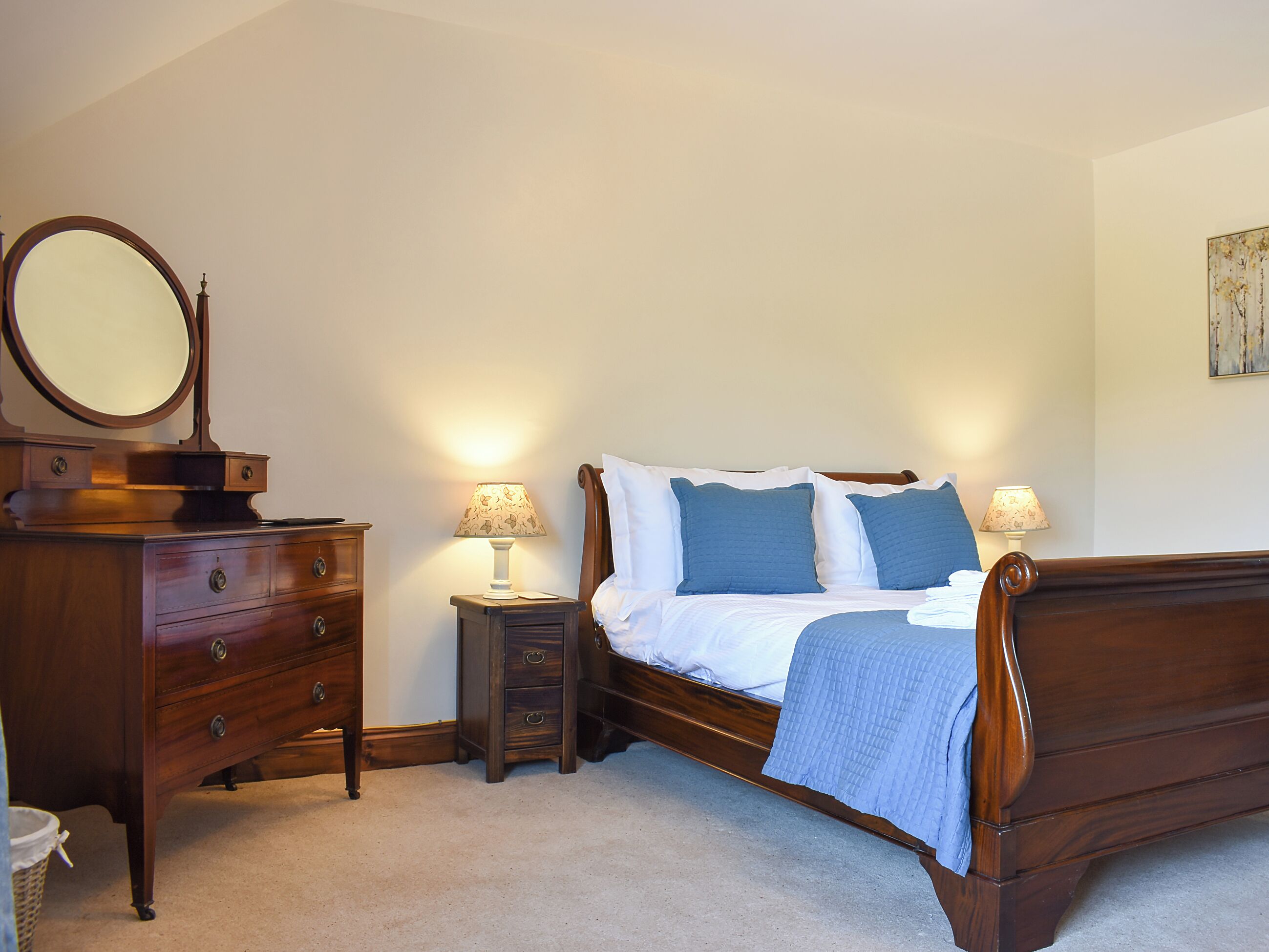 A bedroom with a wooden bed, two bedside tables with lamps, a dresser, and a mirror.