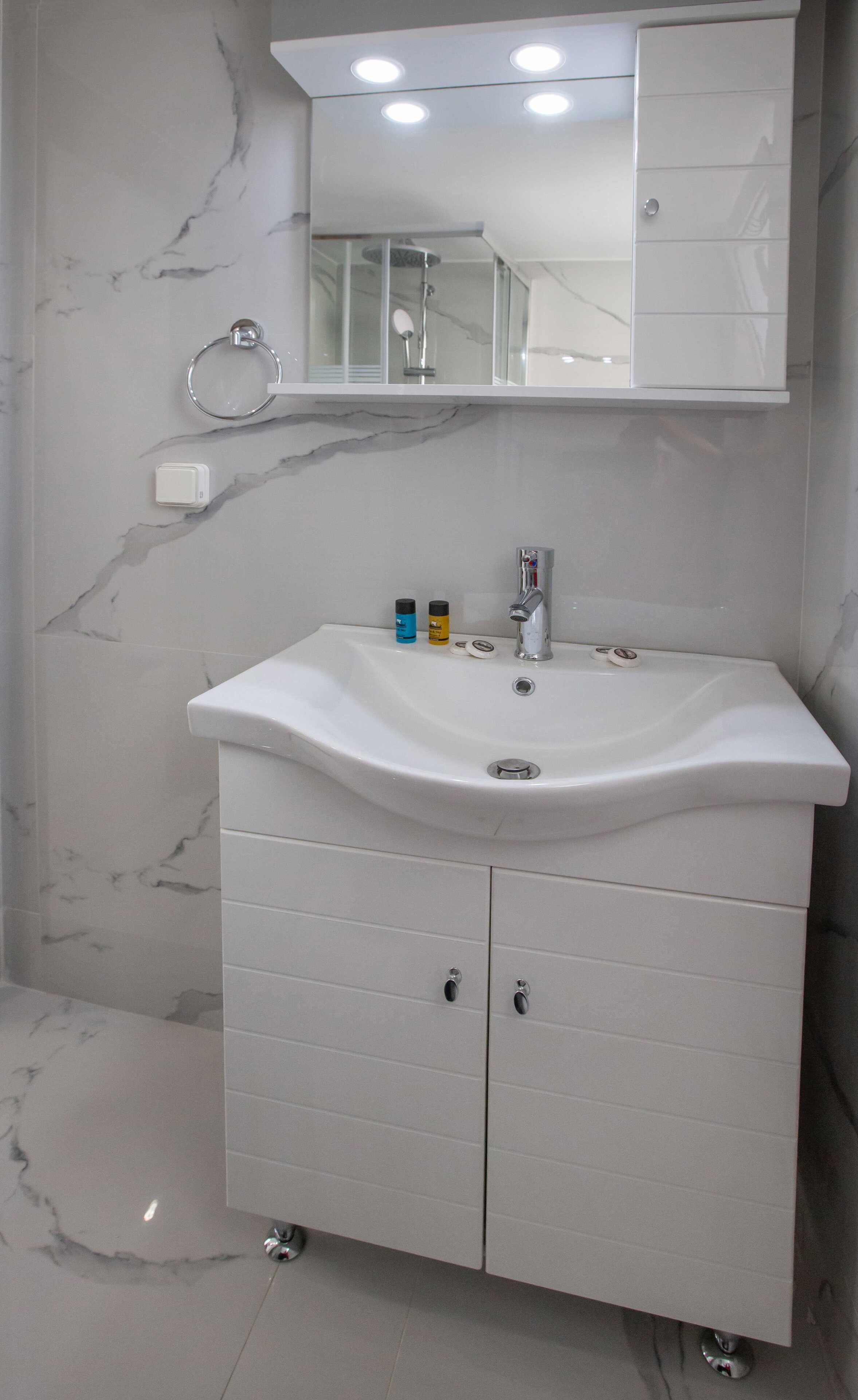 A bathroom with a white marble sink, a mirror above it, and a shower visible through the glass door.